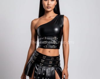 May include: Black one-shoulder crop top and matching pleated mini skirt with buckle and grommet details. The outfit is made of a shiny, faux leather material. The Leather ACreations text is visible on the top.