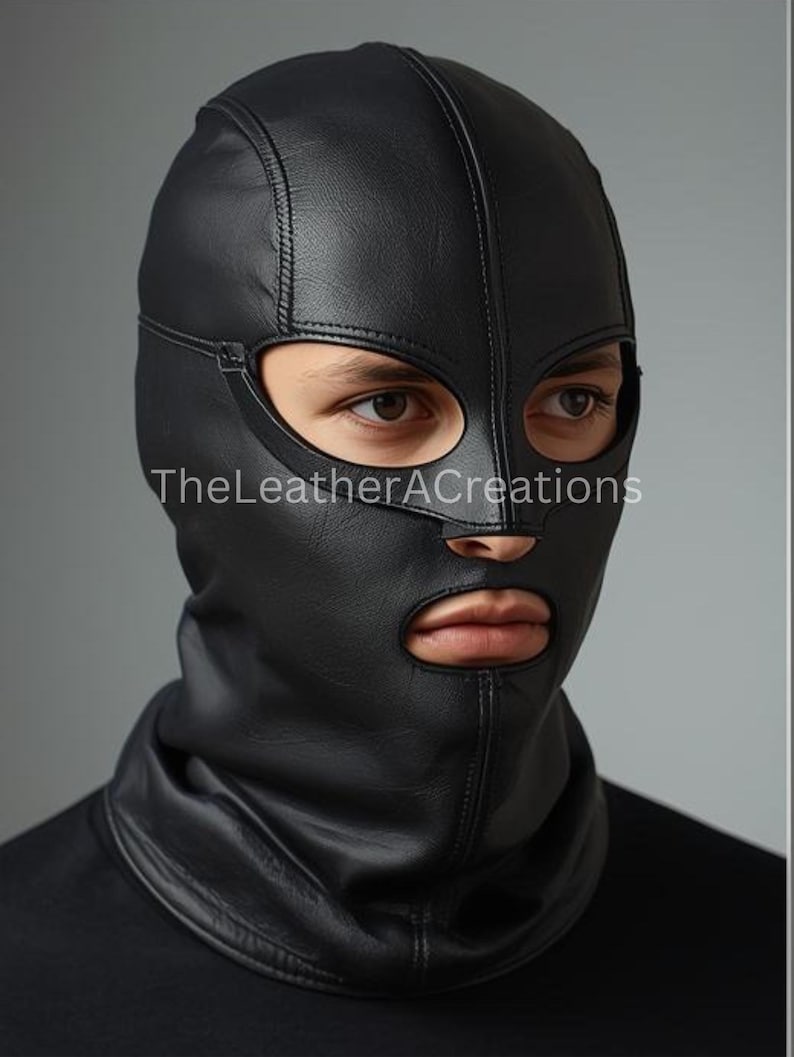 May include: A black leather hood with eye and mouth openings. The hood covers the head and neck, with visible stitching details. The text "TheLeatherACreations" is printed on the lower left side of the hood.