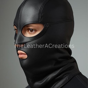 May include: Black leather balaclava with eye and mouth openings. The balaclava features stitched seams and a neck covering. The text "TheLeatherACreations" is visible on the lower part of the balaclava.