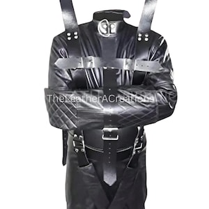 May include: Black leather restraint suit with multiple straps, buckles, and a collar. The suit features quilted arm restraints and leg cuffs. The text "TheLeatherACreations" is visible on the chest.