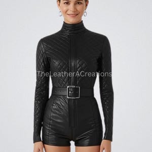 May include: A black leather jumpsuit with a quilted pattern, long sleeves, and a high neckline. The jumpsuit features a front zipper, a belt with a square buckle, and short shorts. The text "TheLeatherACreations" is visible.
