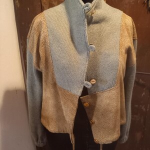 May include: A unique, patchwork-style jacket with a high collar. The jacket features a combination of light blue knit and textured tan panels. It fastens with small, round buttons. The sleeves are long, and the overall design is vintage-inspired.