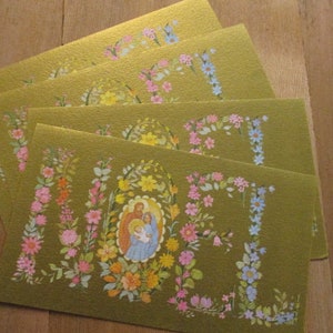Puede incluir: Cuatro tarjetas de felicitaci&oacute;n doradas con dise&ntilde;os florales y una imagen de la Sagrada Familia. Las tarjetas presentan flores coloridas en rosa, azul, amarillo y naranja. Las tarjetas est&aacute;n dispuestas sobre una superficie de madera.