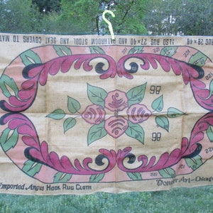May include: Vintage rug cloth with a floral design. The central oval features pink roses and green leaves, surrounded by a border of pink and green stylized leaves. The cloth has text that reads "Imported Angus Hook Rug Cloth" and "Wonder Art - Chicago, Ill."