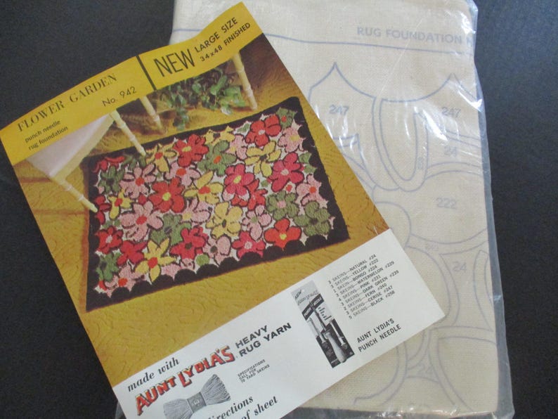 May include: A vintage rug-making kit with a floral design. The kit includes a pattern, yarn, and a punch needle. The pattern shows a finished rug with red, pink, yellow, and green flowers. The rug size is 34 x 48 inches.