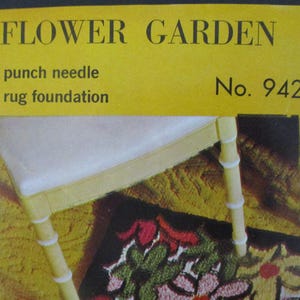 May include: A yellow sign with the words "FLOWER GARDEN" and "punch needle rug foundation." A white chair with yellow legs and a floral rug are visible. The rug features red, green, and pink flowers.