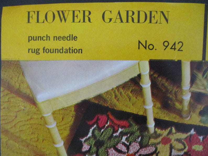 May include: A yellow sign with the words "FLOWER GARDEN" and "punch needle rug foundation." A white chair with yellow legs and a floral rug are visible. The rug features red, green, and pink flowers.