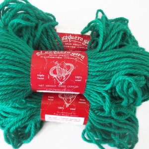 May include: Two skeins of emerald green yarn with red labels. The labels read "el vaquero yarn" and "100% wool". Each skein is labeled as "Net Weight Three Ounces". The yarn is triple twist.
