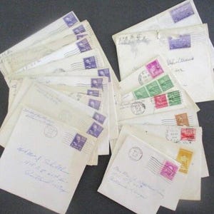 Op de afbeelding: Een verzameling vintage enveloppen, sommige met postzegels in tinten paars, roze, groen en bruin. De enveloppen zijn cr&egrave;mekleurig en voorzien van handgeschreven adressen en poststempels, wat duidt op een historisch thema.