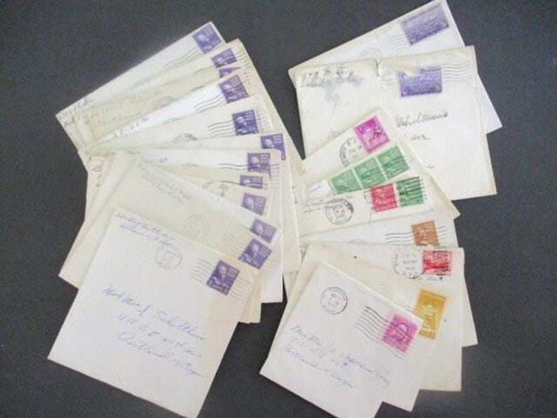 Op de afbeelding: Een verzameling vintage enveloppen, sommige met postzegels in tinten paars, roze, groen en bruin. De enveloppen zijn cr&egrave;mekleurig en voorzien van handgeschreven adressen en poststempels, wat duidt op een historisch thema.