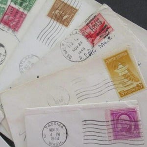 Op de afbeelding: Een verzameling vintage enveloppen met diverse postzegels en poststempels. De enveloppen zijn wit en cr&egrave;mekleurig, met postzegels in groen, bruin en paars. Poststempels tonen data en locaties zoals Los Angeles en Tacoma.