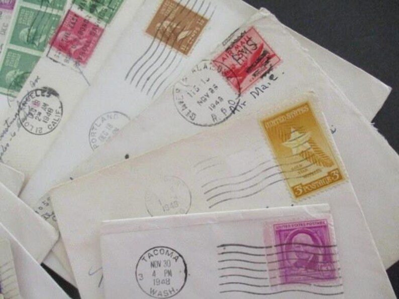 Op de afbeelding: Een verzameling vintage enveloppen met diverse postzegels en poststempels. De enveloppen zijn wit en cr&egrave;mekleurig, met postzegels in groen, bruin en paars. Poststempels tonen data en locaties zoals Los Angeles en Tacoma.