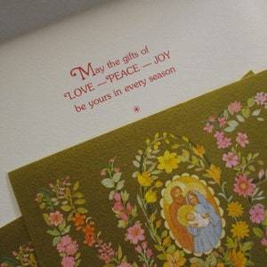 Puede incluir: Una tarjeta de Navidad con un dise&ntilde;o floral y el texto "Que los dones de AMOR - PAZ - ALEGR&Iacute;A sean tuyos en cada estaci&oacute;n." La tarjeta presenta una ilustraci&oacute;n de la Sagrada Familia.