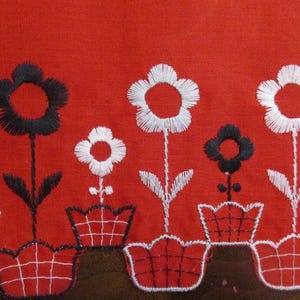 以下が含まれることがあります： 赤い生地に刺繍された花柄のクローズアップ。デザインは、茶色のベースに赤いポットに入った、交互に配置された黒と白の花が特徴です。花には詳細な花びらと茎があります。