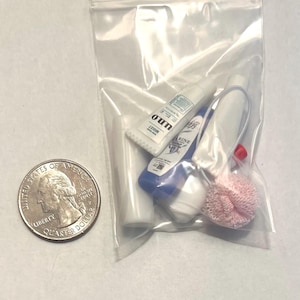 以下が含まれることがあります： ミニチュアのトイレタリーが入った透明なビニール袋。チューブとピンクのスポンジが含まれています。サイズの比較のために、バッグの隣に米国の25セント硬貨があります。チューブにはテキストが書かれた白と青のラベルが付いています。