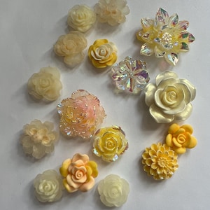 May include: A collection of various floral embellishments in shades of yellow, cream, and iridescent finishes. The assortment includes rose and daisy designs, perfect for crafting or adding decorative accents to projects.