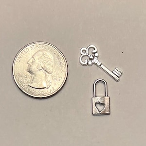 May include: Silver-colored charms including a key, a padlock with a heart cutout, and a quarter coin. The key has ornate detailing, and the padlock is small. The quarter coin is on the left side of the image.