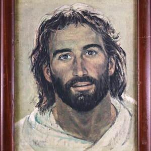 May include: A framed portrait painting of a person with shoulder-length brown hair, a full beard, and blue eyes, wearing a white garment. The artwork is enclosed in a dark brown wooden frame and features the signature P. Hook in the lower left corner.