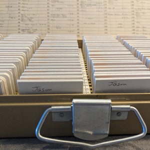 May include: A metal box with a handle and a latch. The box is filled with small white cards. The cards have the name "Jason" written on them.