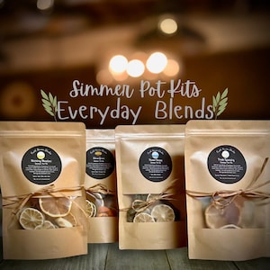 May include: Four brown paper pouches tied with twine, each containing dried citrus slices and herbs. The pouches are labeled "Morning Meadow", "Citrus Grove", "Ocean Breeze", and "Fresh Sparling". The text "Simmer Pot Kits Everyday Blends" is above the pouches.
