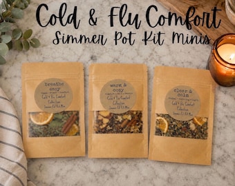 May include: Three brown paper pouches labeled Cold & Flu Comfort Simmer Pot Kit Minis. Each pouch features a circular sticker with text: breathe easy, warm & cozy, or clear & calm. The clear windows reveal dried orange slices and spices.