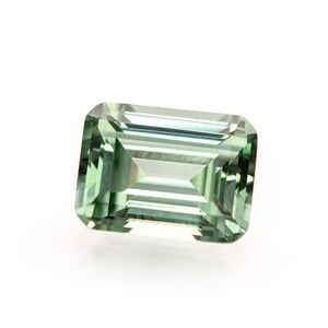 May include: A rectangular-cut, pale green gemstone with a faceted surface. The gem is set against a white background, highlighting its clarity and colour. The gemstone's facets reflect light, creating a sparkling effect.