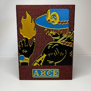 May include: A burgundy box featuring a character design with gold, black, and blue accents. The design includes a hat, a hand with a flame, and the word "ACE" in a blue rectangle.