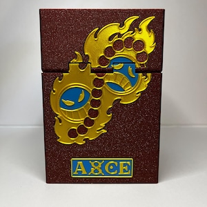 May include: A burgundy box with a gold and blue design. The box has a hinged lid and the word "ACE" in blue letters. The design is a stylized flame and gear motif.
