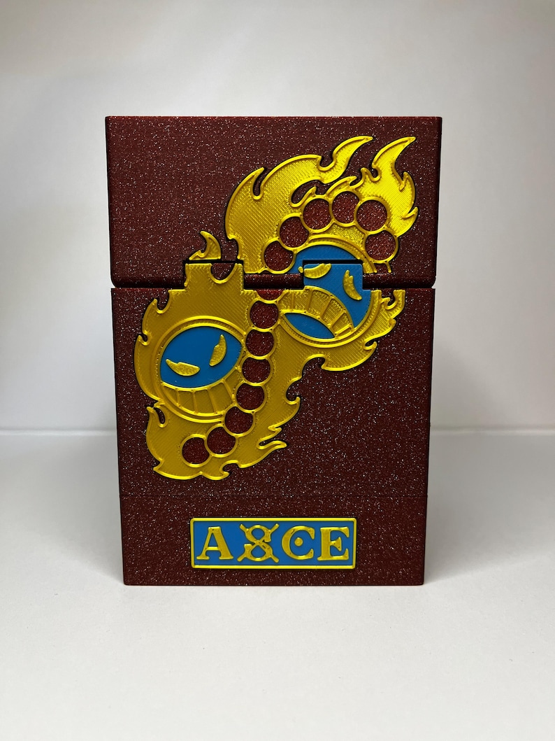 May include: A burgundy box with a gold and blue design. The box has a hinged lid and the word "ACE" in blue letters. The design is a stylized flame and gear motif.
