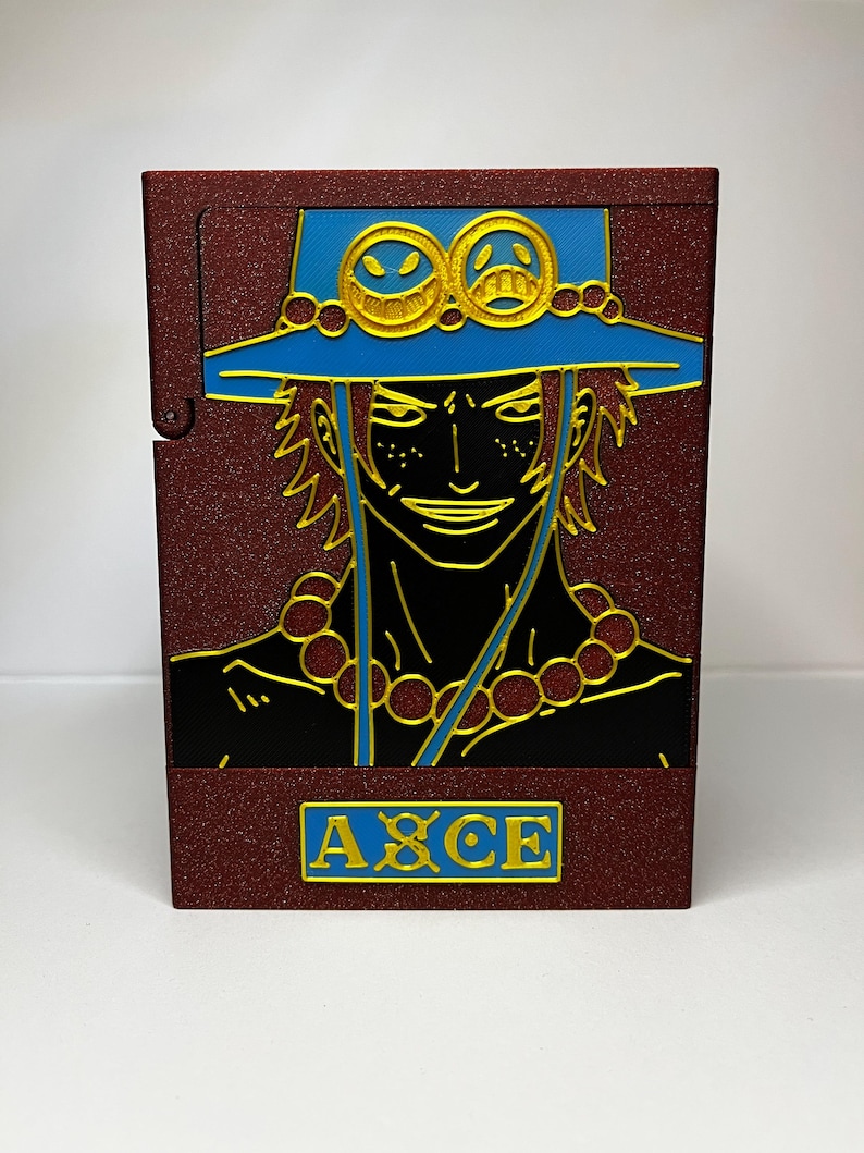 May include: A maroon cigarette case featuring a detailed illustration of a character with a blue hat and gold accents. The character's face is black with gold outlines, and the word "ACE" is displayed in a gold rectangle.