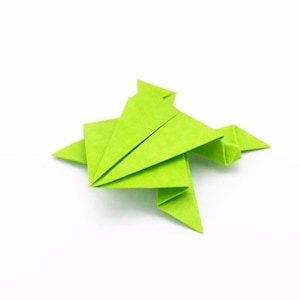 May include: A bright green origami frog, crafted from folded paper, sits on a white surface. The frog's form is angular, with visible creases and points, showcasing the art of paper folding. The frog is a symbol of good luck.