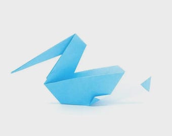 May include: A light blue origami pelican, crafted from folded paper, is depicted against a white background. The pelican's beak is extended, and its body is angular, showcasing the art of paper folding. A small triangle is next to the pelican.