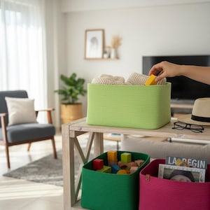 May include: A light green rectangular storage basket filled with beige items. Below, a green basket holds colourful wooden blocks, and a pink basket contains a magazine. The baskets are on a wooden shelf in a living room.
