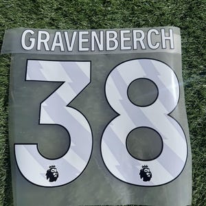 May include: A clear, transparent sheet with the name "GRAVENBERCH" above the number "38". The numbers are white with a gray, diagonal striped pattern and a black outline. The Premier League logo is at the bottom.