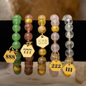 May include: Five beaded bracelets with gold-colored accents and hexagonal charms. The bracelets feature green, brown, gold, pink, and clear beads. Each charm displays a number: 888, 777, 520, 222, and III.