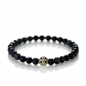 May include: A dark blue beaded bracelet with a silver-colored, decorative centerpiece. The bracelet features faceted, round beads and a detailed, spherical accent. The beads appear to be approximately 0.3 inches in diameter.