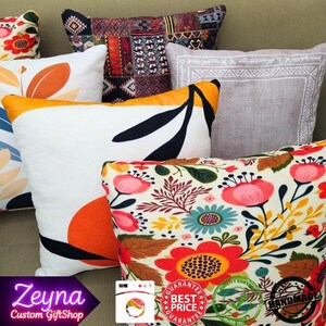 May include: A collection of decorative throw pillows with various patterns. Pillows feature floral, geometric, and abstract designs in colors like orange, white, black, and red. Some pillows have a yellow border. The image includes the text "Zeyna Custom GiftShop".