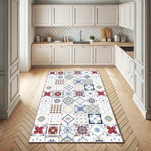 May include: A rectangular area rug with a colorful tile pattern in a kitchen setting. The rug features a mix of geometric and floral designs in shades of red, blue, yellow, and white. The kitchen has white cabinets and wooden floors.