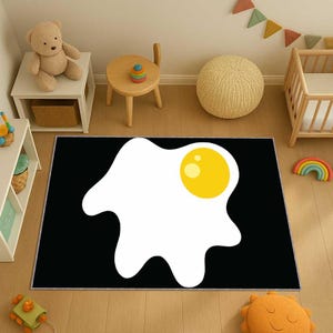 May include: A rectangular black rug with a large, cartoon-style fried egg design. The egg has a white yolk and a bright yellow yolk. The rug is placed on a wooden floor in a child's room.
