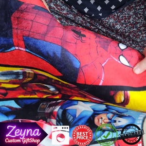 May include: A colorful blanket featuring illustrations of Marvel superheroes, including Spider-Man and Captain America. The blanket has a red, blue, and yellow color scheme. The text "Zeyna Custom GiftShop" is visible in the corner.
