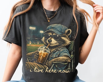 Ahora vivo aquí. Camiseta oscura divertida con mapache y estampado de campo de béisbol. Regalo para el día del partido de béisbol o sóftbol.