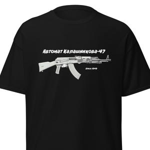 Puede incluir: Camiseta negra con un gráfico blanco de un rifle de asalto AK-47. El texto "Автомат Калашникова-47" está encima del rifle, con "Since 1949" debajo. La camiseta es de cuello redondo.