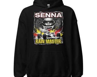Puede incluir: Sudadera con capucha negra con un gráfico de un coche de carreras de Fórmula 1 y el texto "SENNA RAIN MASTER". El diseño incluye un retrato de un piloto con casco, con acentos amarillos, rojos y blancos.