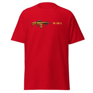 May include: A red t-shirt with a detailed illustration of a yellow and black SCAR-L rifle. The text "SCAR-L" is printed in yellow. The shirt is made of a soft material. The design is on the front.