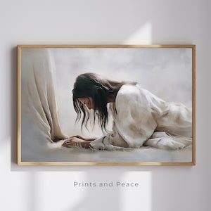 Puede incluir: Una impresión enmarcada que representa a una persona con una túnica blanca arrodillada con la cabeza inclinada. La obra de arte utiliza una paleta de colores suaves y apagados, centrándose en la luz y la sombra. El texto "Prints and Peace" está impreso en la parte inferior del marco.