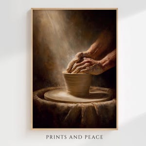 Puede incluir: Una impresión enmarcada que representa manos moldeando una vasija de arcilla en un torno de alfarero. La obra de arte está en tonos cálidos y terrosos con un efecto de foco. El texto "PRINTS AND PEACE" está en la parte inferior del marco.