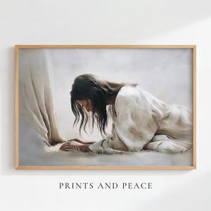 May include: A framed horizontal wall art print depicting a person with long dark hair kneeling in a white robe on a light surface, with the lower portion of another figure in a white robe visible to the left. The text PRINTS AND PEACE is below.