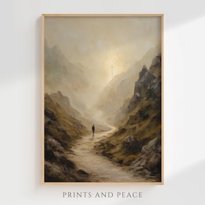 Puede incluir: Una impresión enmarcada de un paisaje con una persona caminando por un camino en un valle de montaña. La obra de arte utiliza una paleta de colores apagados de marrones, beiges y amarillos, con una cruz a lo lejos. El texto "PRINTS AND PEACE" está en la parte inferior.