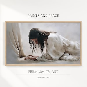 May include: A framed digital artwork titled PRINTS AND PEACE PREMIUM TV ART 3840X2160. The image depicts a person with long dark hair wearing a white robe, kneeling on the ground in a humble posture, rendered in a soft, painterly style.