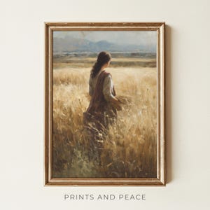 May include: A framed print of a woman in a wheat field. The artwork depicts a woman in a long dress and shawl, holding wheat. The background shows a field of wheat and mountains. The frame is gold. The text "PRINTS AND PEACE" is at the bottom.